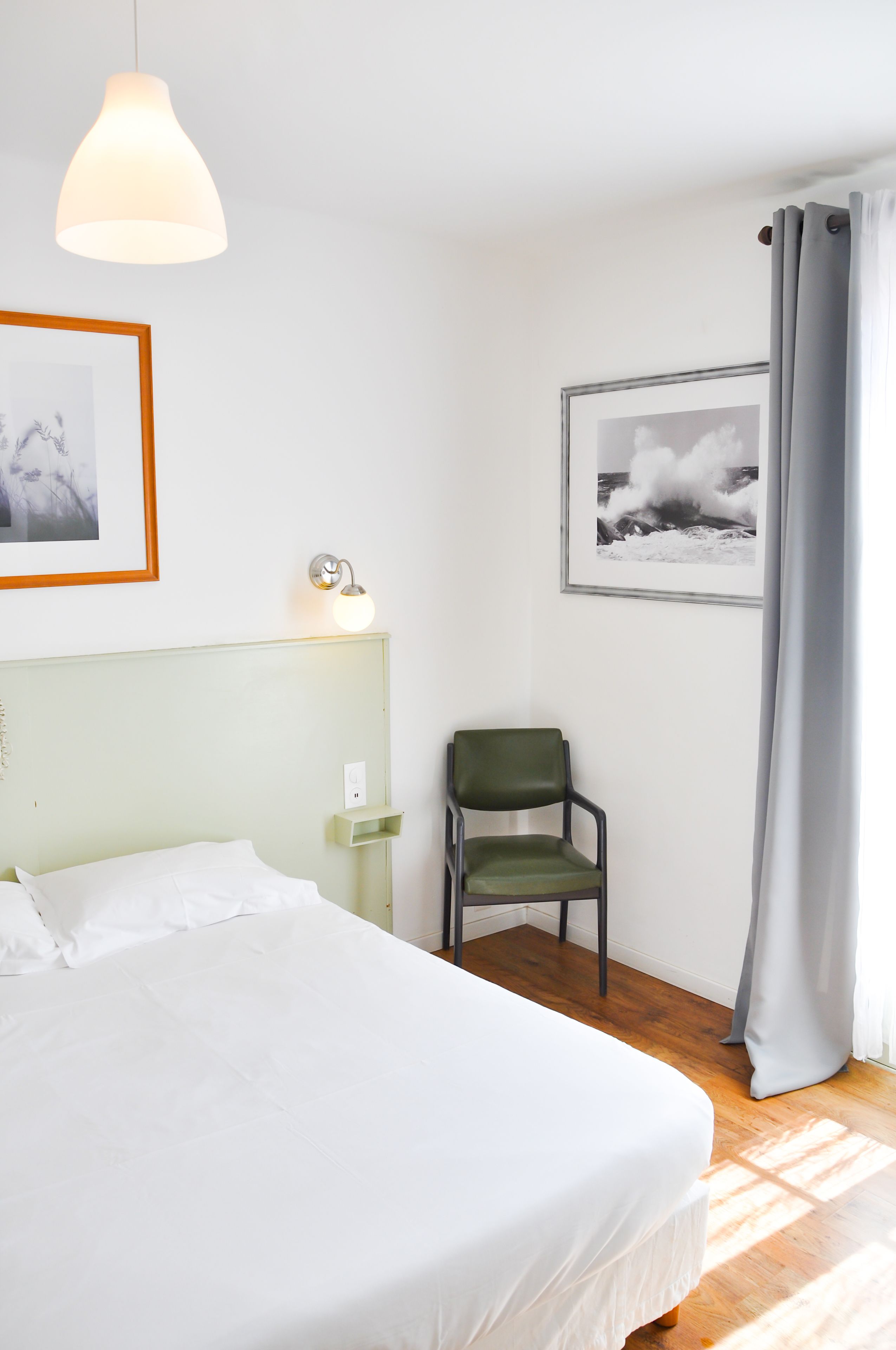 Ein Hotelzimmer mit einem Bett, einem Sessel, einer Wandlampe und zwei gerahmten Bildern.