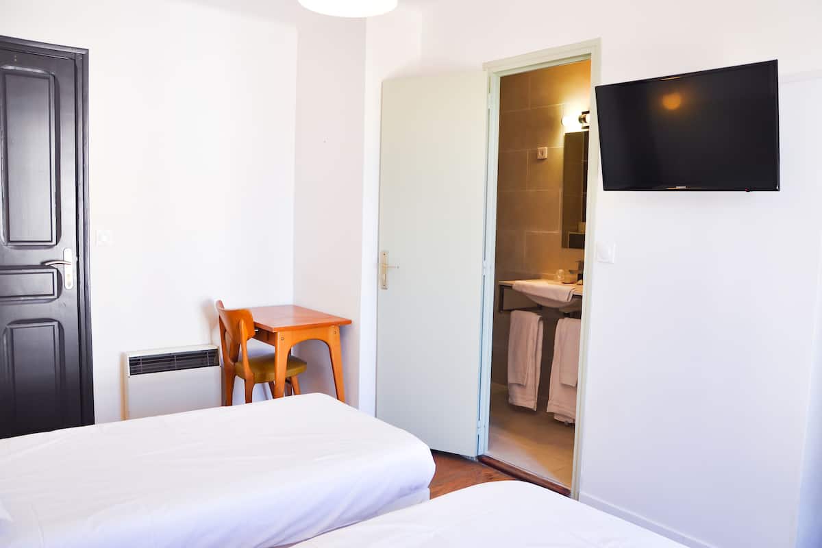 Une chambre d’hôtel avec un lit, un bureau, une chaise, une télévision et une salle de bain visible à travers une porte ouverte.