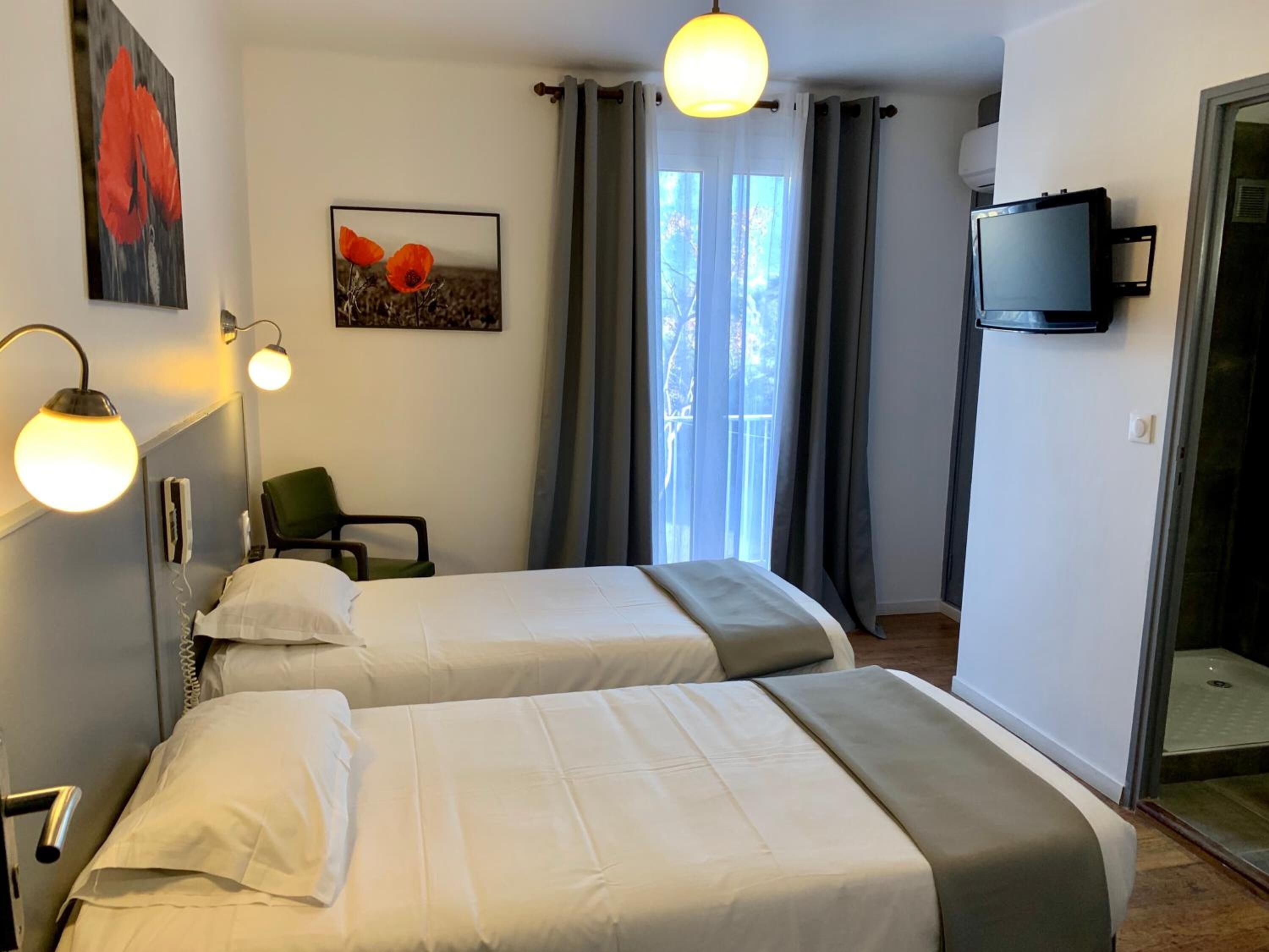 A hotel room with two beds, a TV, a painting, and a window with curtains.