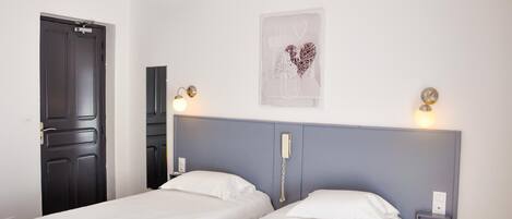 A hotel room with two single beds, a dark door, a light switch, and a wall-mounted phone.