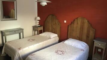 A room with two beds, a wooden headboard, a bedside table with a lamp, and a mirror on the wall.