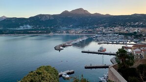 Una marina costera con barcos amarrados, un muelle y montañas al fondo.