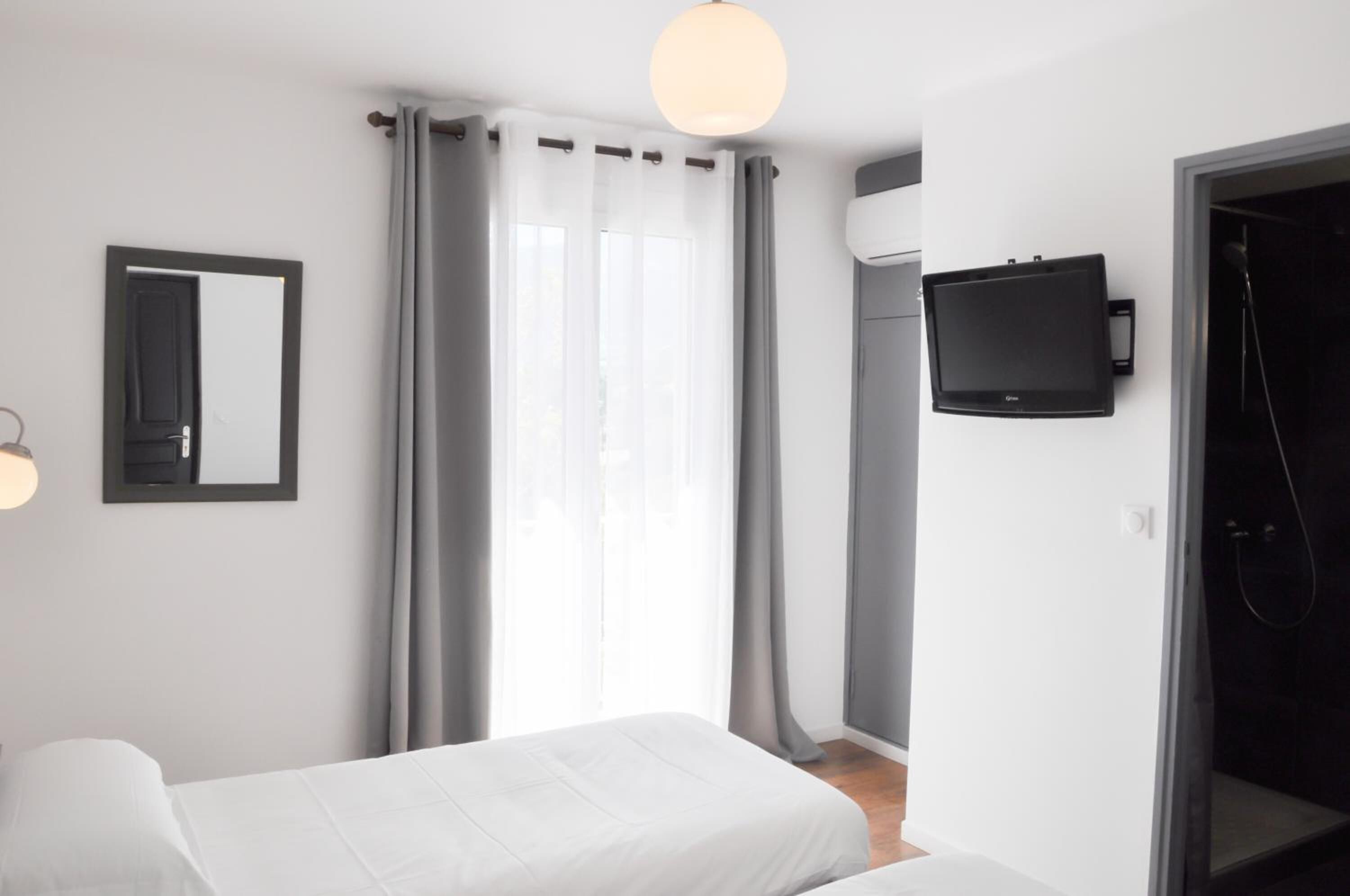 Una habitación de hotel moderna con una cama, televisión, ducha y un amplio ventanal con cortinas.