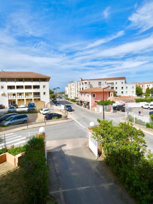 A street view of a residential area with multi-story buildings, a parking lot, and a gated entrance. - Hôtel Les Arbousiers (Calvi)