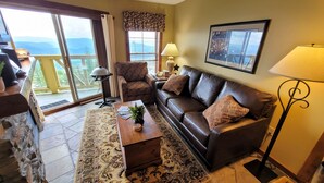 A living room with a sofa, armchair, coffee table, and a large window offering a view of the outdoors. - TOP FLOOR IN RIMFIRE/VILLAGE! NEVER RENTED BEFORE JULY 2022 2 BEDROOMS SLEEPS 8! (Snowshoe)