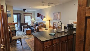A spacious living area with a sofa, chairs, and a coffee table. There is a kitchen area with a sink, stove, and cabinets. - TOP FLOOR IN RIMFIRE/VILLAGE! NEVER RENTED BEFORE JULY 2022 2 BEDROOMS SLEEPS 8! (Snowshoe)