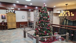 A Christmas tree in a lobby with stone walls, a wooden bench, and a chandelier. - TOP FLOOR IN RIMFIRE/VILLAGE! NEVER RENTED BEFORE JULY 2022 2 BEDROOMS SLEEPS 8! (Snowshoe)