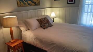 A neatly made bed with white linens, a wooden nightstand with a lamp, and a painting on the wall.