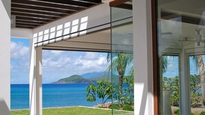Une chambre moderne dotée de grandes fenêtres en verre offrant une vue sur l’océan et un paysage tropical.