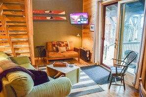 A cozy living room with a sofa, a wooden ladder, a television, and a view through a glass door.