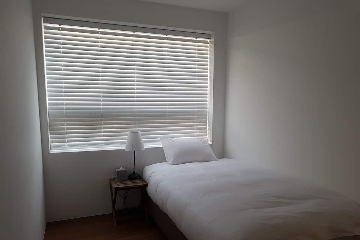 A bedroom with a bed, a bedside table with a lamp, and a window with blinds.