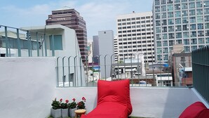 A rooftop terrace with red seating, a small table, and potted plants. - Hostel Single Single (Busan)