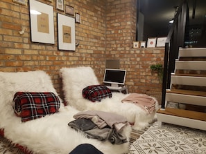 Ein gemütliches Zimmer mit Backsteinwand, einem weißen, flauschigen Bett, einem Flachbildfernseher und einer Treppe.