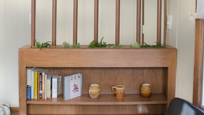 Una estantería de madera con libros y objetos decorativos, una silla negra y una pequeña mesa con una taza y platillo.