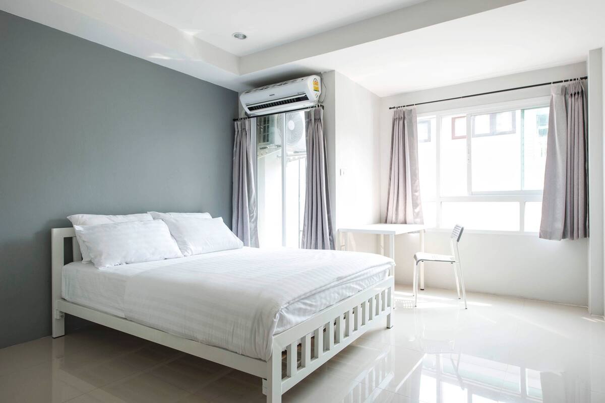 Een moderne slaapkamer met een bed, airconditioning en een klein tafeltje met een stoel.