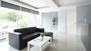 Ein modernes Wohnzimmer mit einem schwarzen Ledersofa, einem weißen Couchtisch und einem großen Fenster mit Blick auf die Straße.