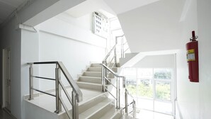 Eine moderne Treppe mit Metallgeländern, ein Rauchmelder an der Wand und ein Fenster mit Blick ins Grüne.
