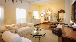 A living room with a sofa, armchairs, a glass coffee table, a wooden side table, and a dining area with a chandelier. - Luxury Cottage in Jacksonville's Historic Core! (Jacksonville)
