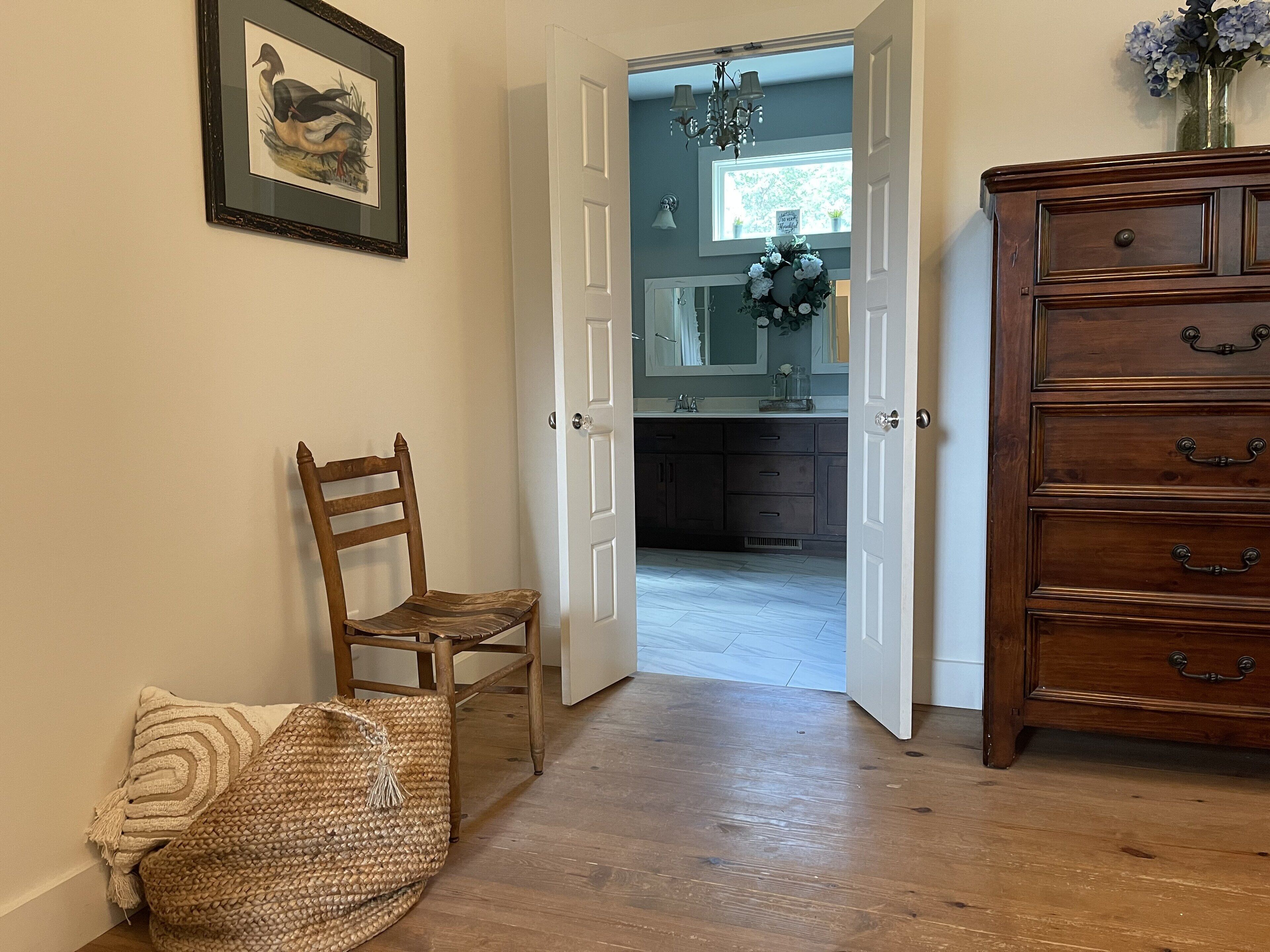 A hallway with a wooden chair, a woven bag, and a wooden dresser.
