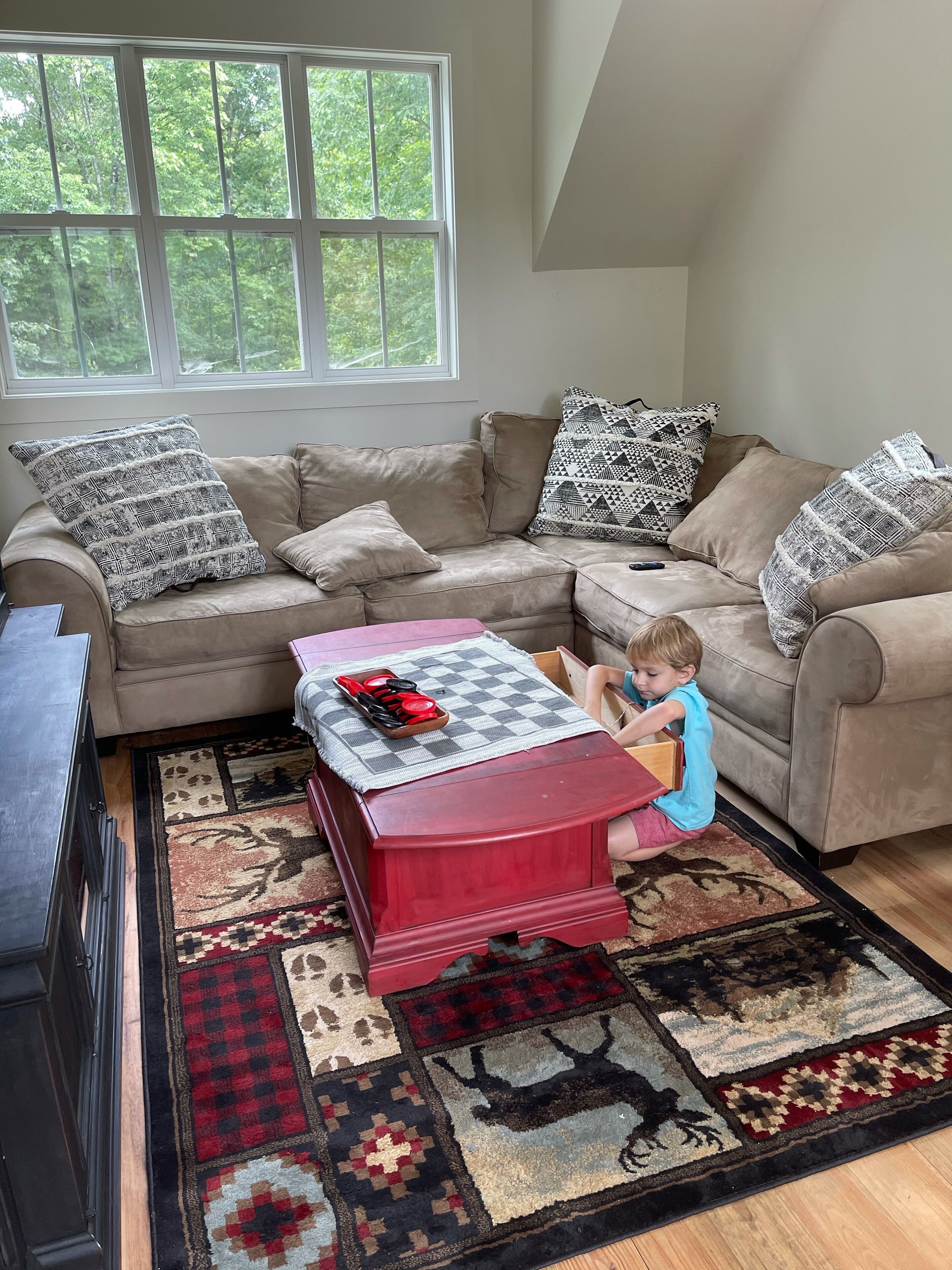 A living room with a sectional sofa, a red coffee table, and a patterned rug.