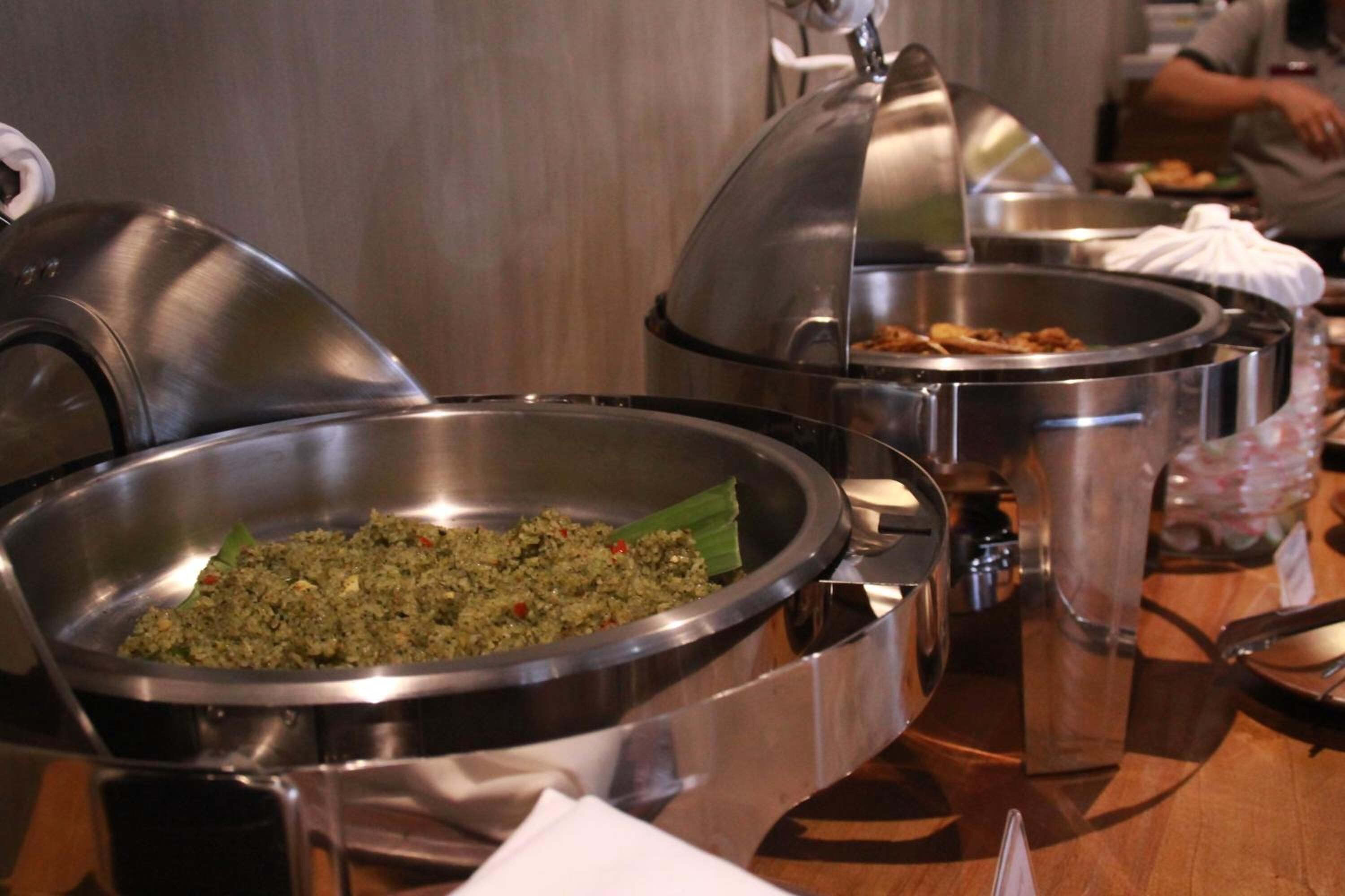 A buffet table with various food dishes in stainless steel bowls.
