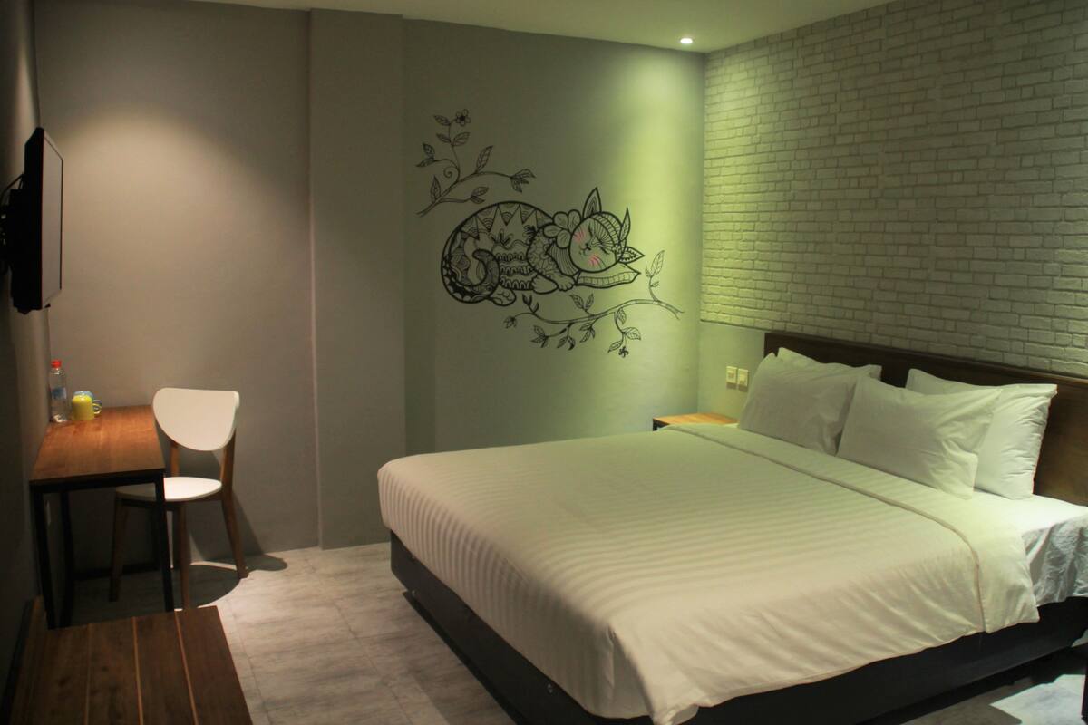 Un dormitorio con cama, una silla, una mesita y un adorno en la pared.