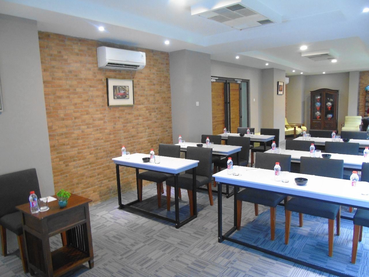 A conference room with multiple tables and chairs, air conditioning units, and a brick wall.