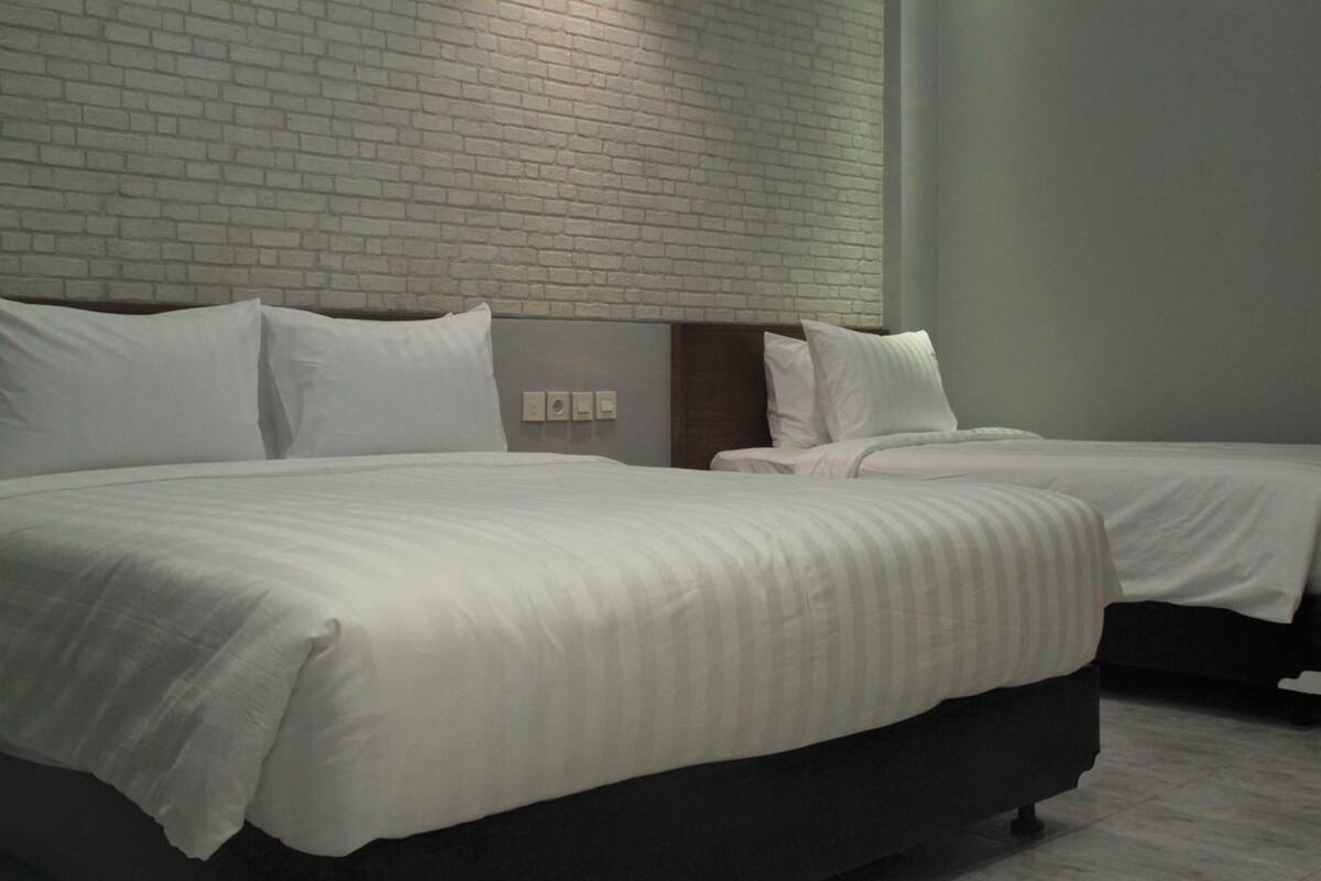 Una habitación de hotel con dos camas, un muro de ladrillo y una pared blanca lisa.