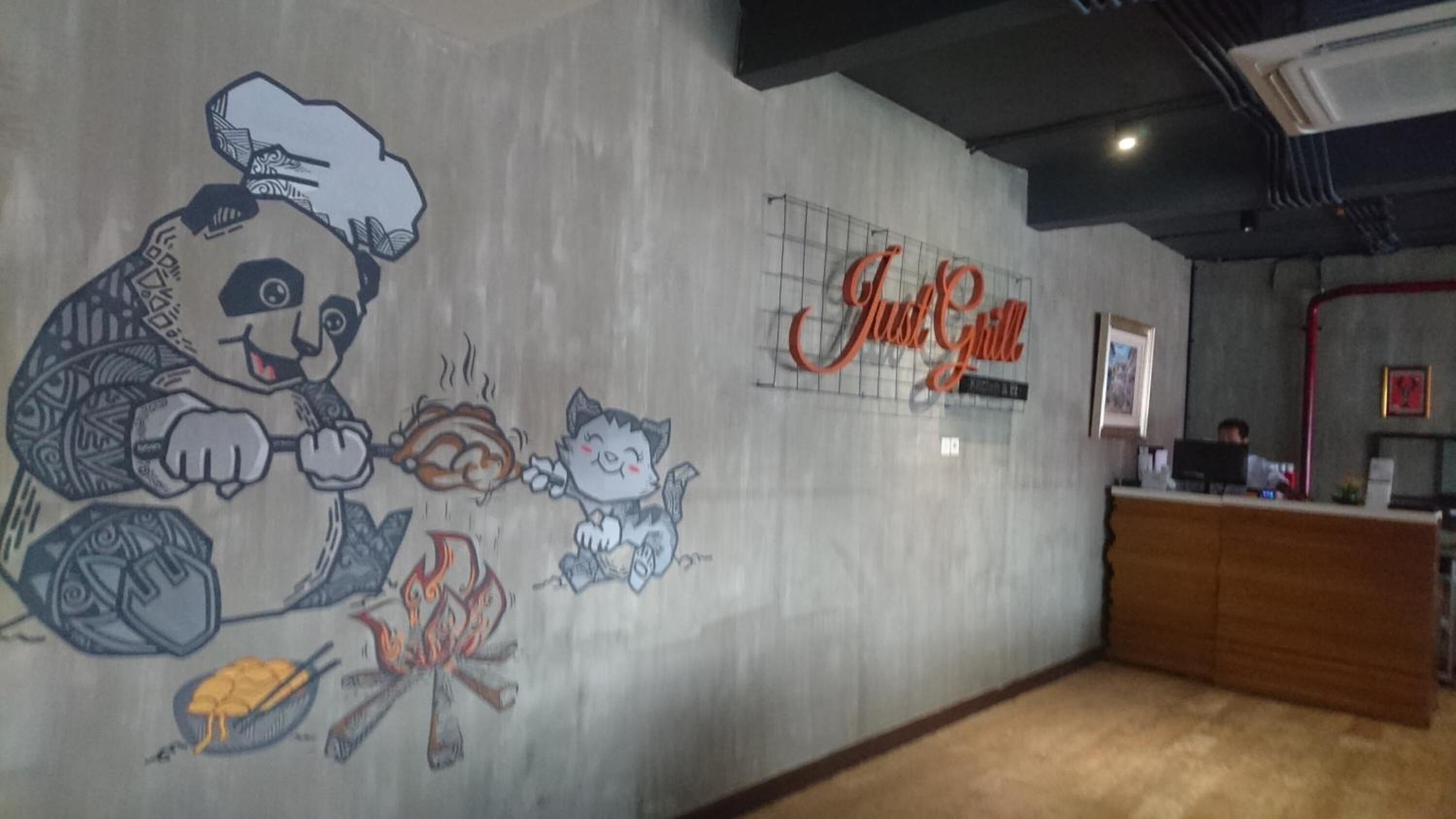 A restaurant interior with a mural of a chef and a cat, a sign reading "Just Grill," and a reception desk.