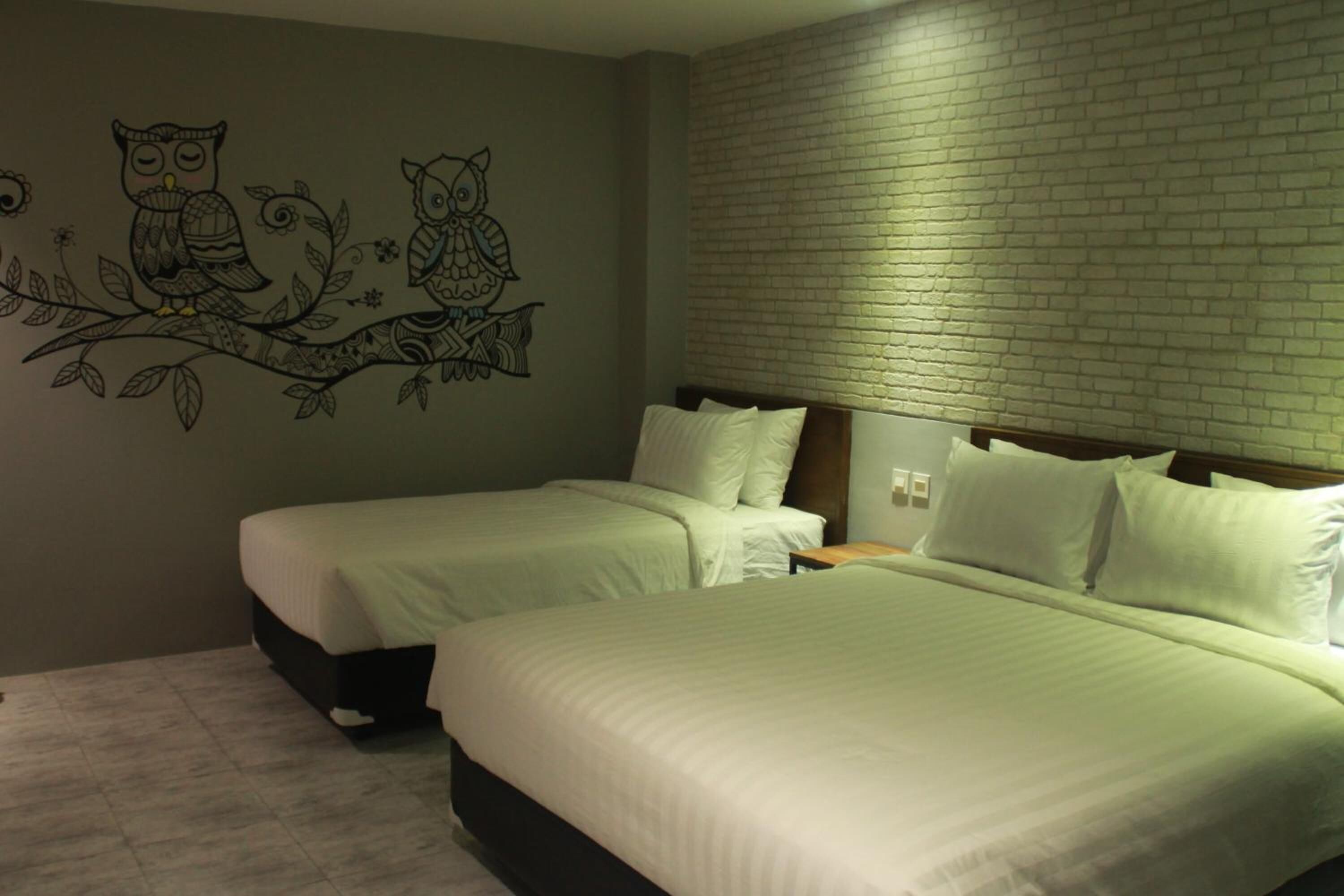 A hotel room with two beds, a brick wall, and a mural of owls on the wall.