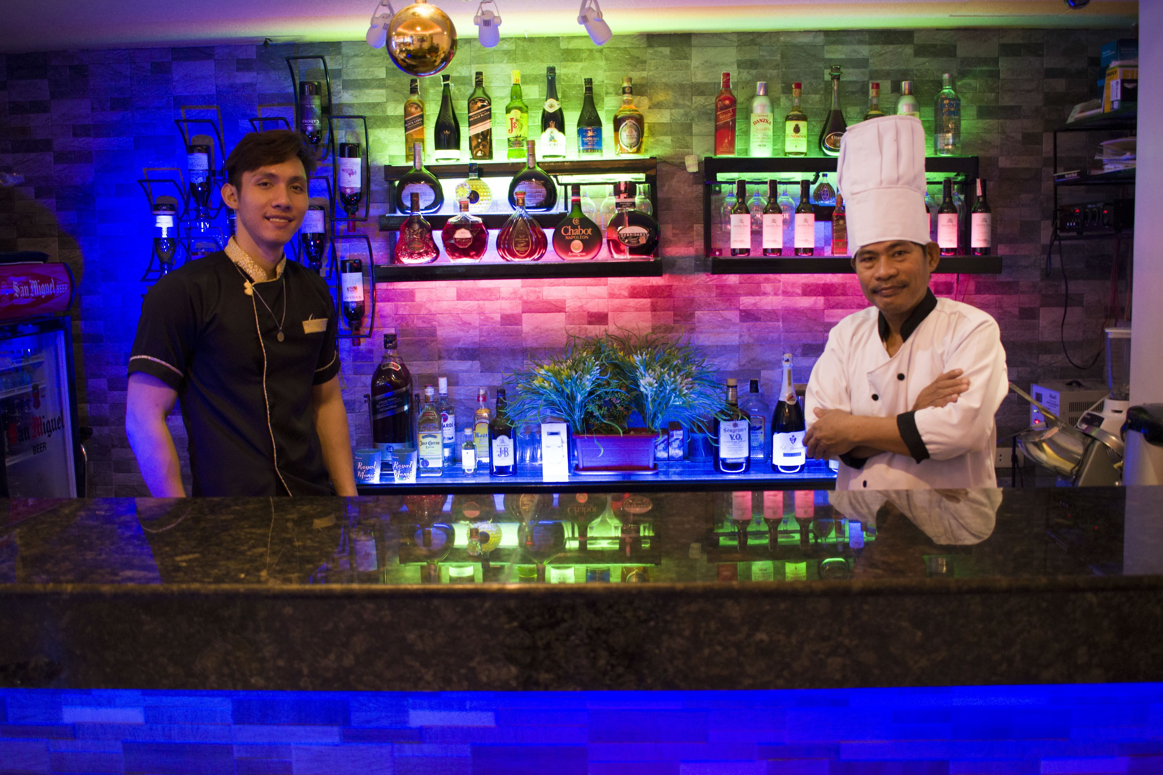 A bar area with a counter, shelves of bottles, and a decorative plant.