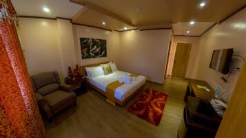Habitación de hotel con cama, una silla, escritorio, televisión y un cuadro en la pared.