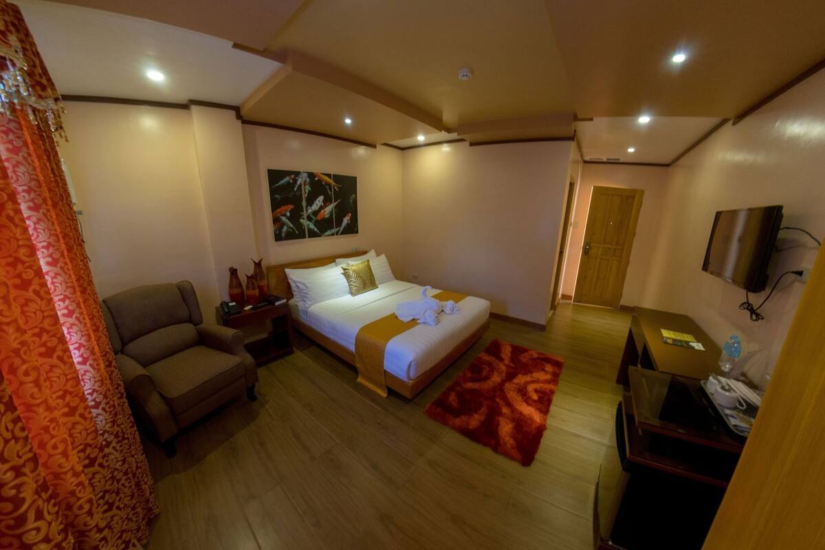 A hotel room with a bed, a desk, a chair, a TV, and a painting on the wall.