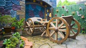 A rustic wooden carriage with large wheels, positioned in front of a stone wall with a colorful, textured design. - Royal Mansion Hotel (Tabaco City)