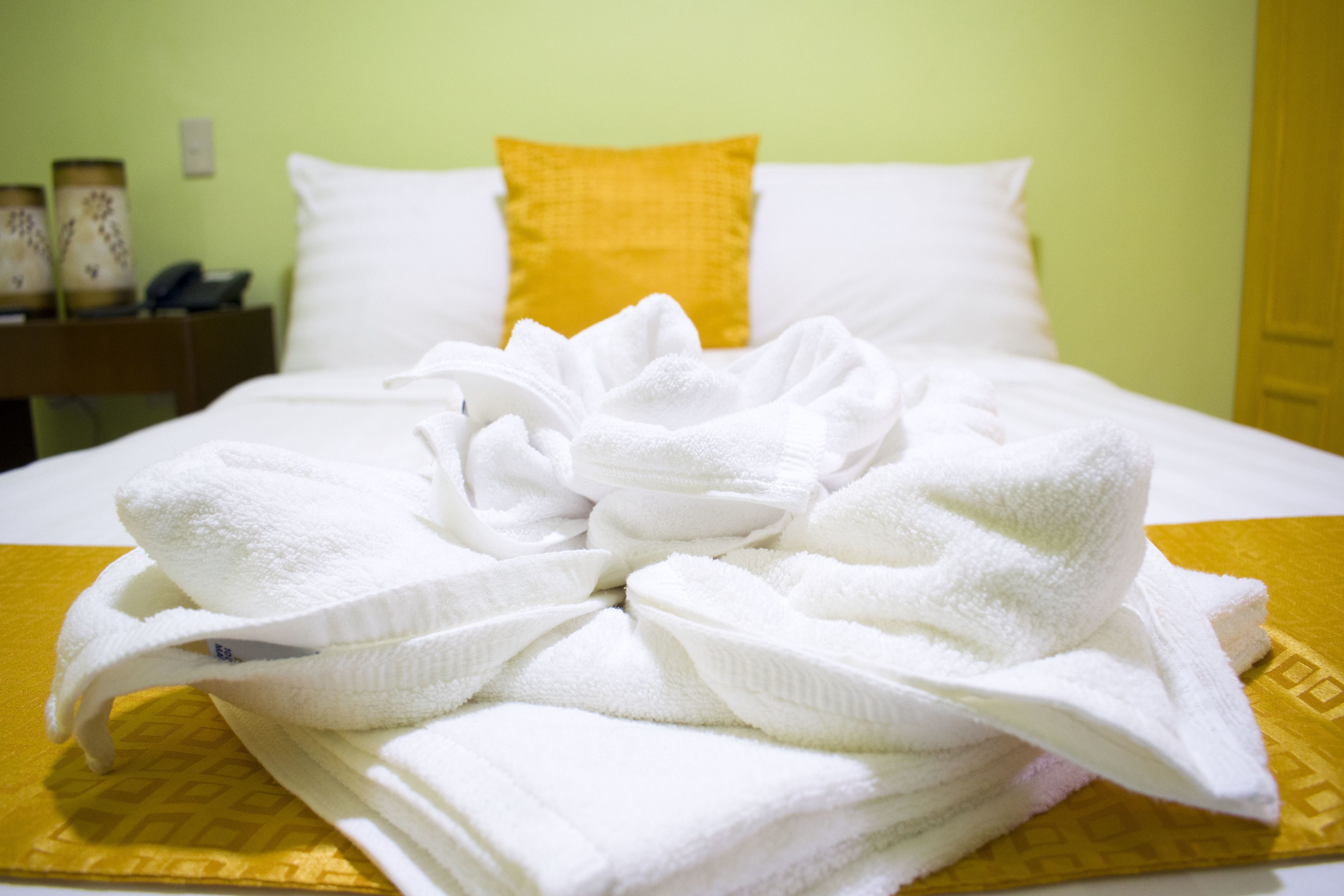 A neatly made bed with a white and yellow bedspread, a yellow pillow, and a folded white towel on the bed.