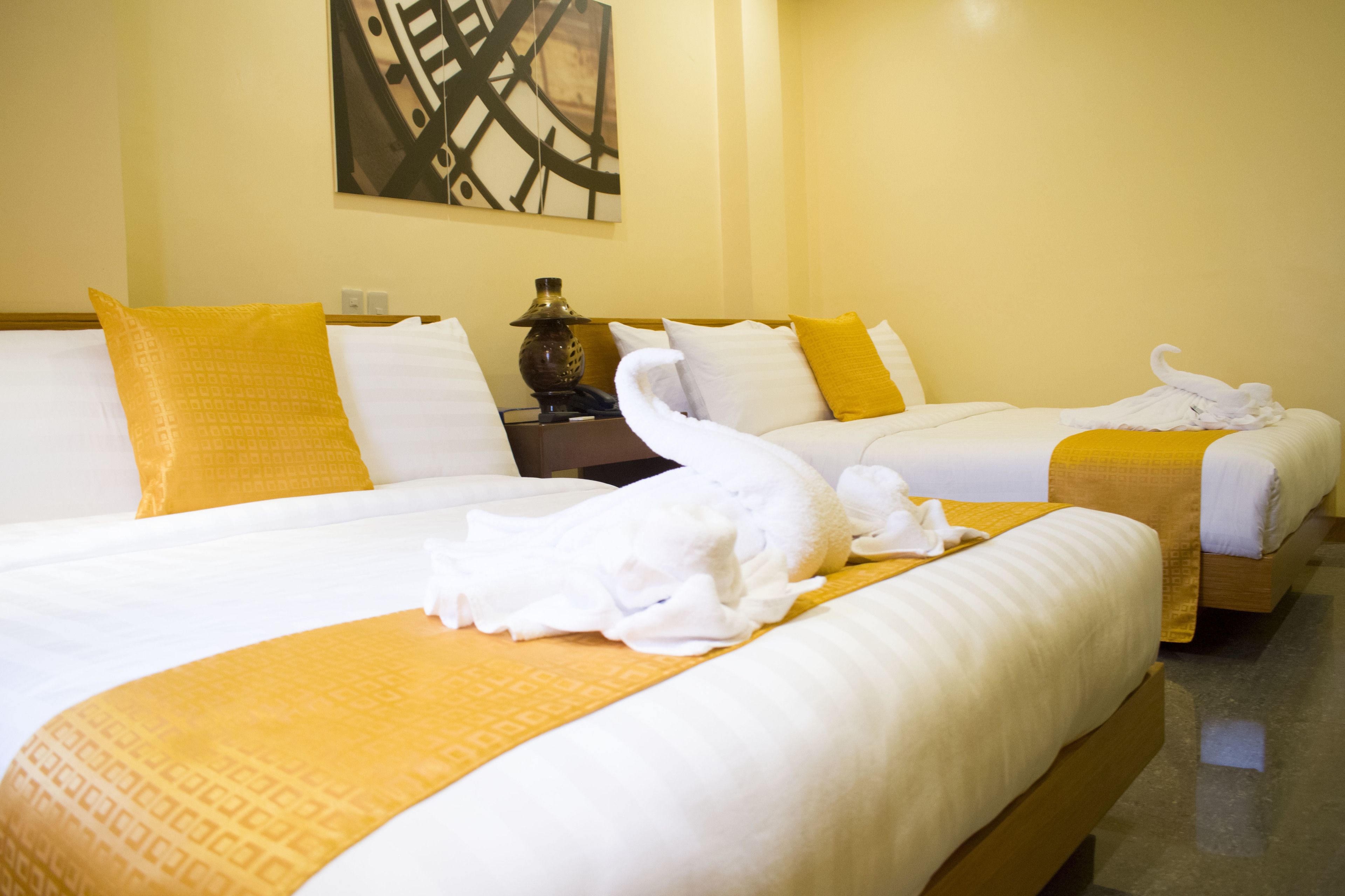 Une chambre d’hôtel avec deux lits, chacun agrémenté de draps blancs et de touches de couleur jaune, ainsi qu’une lampe sur une table de chevet.