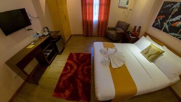 A hotel room with a bed, a desk, a chair, a TV, a wardrobe, and a window with curtains.
