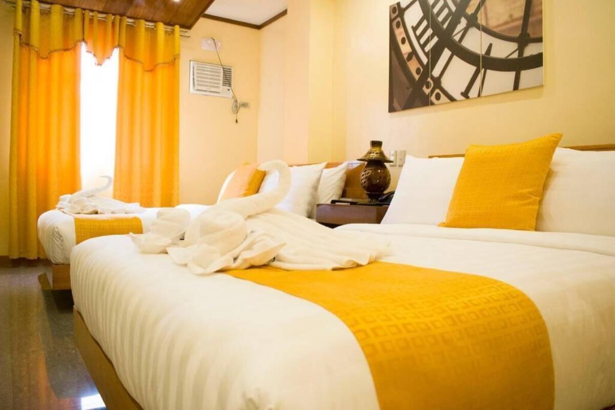 A hotel room with two beds, a large painting on the wall, and a window with curtains.
