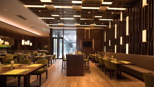 Un restaurante moderno con suelo de madera, sillas tapizadas en verde y una zona de bar central.