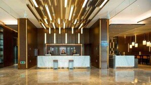 Un moderno vestíbulo de hotel con mostrador de recepción, suelo de mármol y una lámpara colgante.