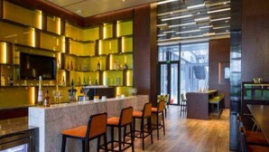 Zona de bar moderna con mostrador de mármol, diversas opciones de asientos y un amplio ventanal que proporciona luz natural.