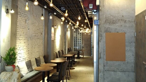 A modern interior with exposed brick walls, hanging pendant lights, and a mix of seating options including tables and a bench. - DAN Hostel (Taipei)