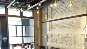 A modern interior with a brick wall, leather sofa, wooden chairs, and hanging light bulbs. - DAN Hostel (Taipei)