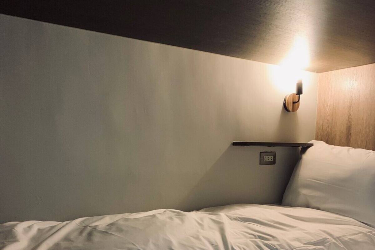 A single bed with white bedding in a room with a wooden headboard and a wall-mounted light fixture.
