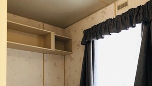 A small, compact room with two beds, a window with curtains, and a headboard.