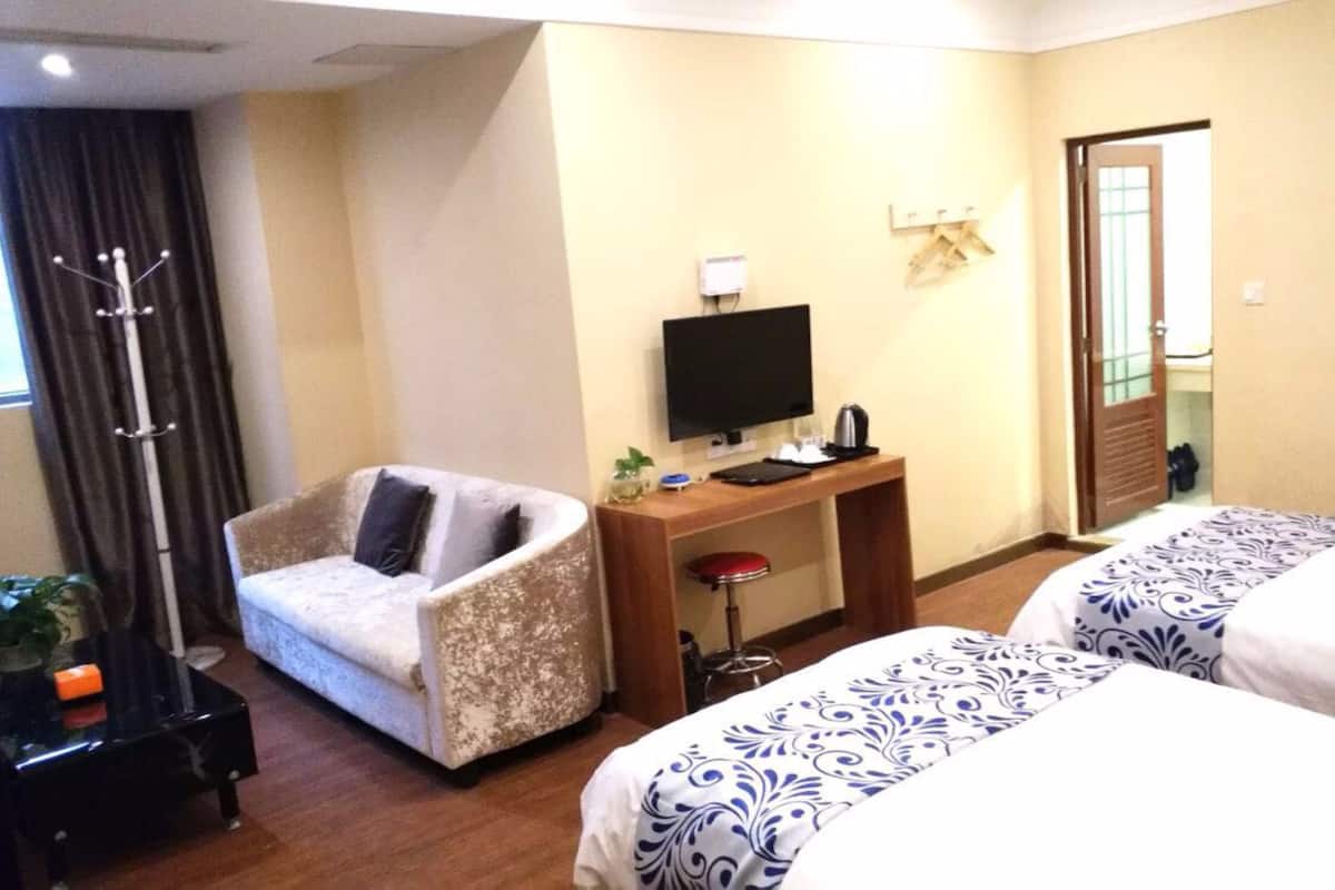 A hotel room with a sofa, a desk with a TV, and two beds.