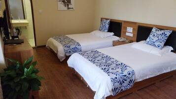 A hotel room with two beds, a wooden floor, a potted plant, and a painting on the wall.