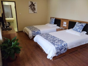 Habitación de hotel con dos camas, suelo de madera, una planta en maceta y un cuadro en la pared.