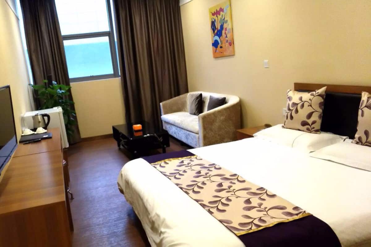 A hotel room with a bed, a chair, a desk with a coffee maker, a TV, and a painting on the wall.