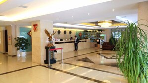 Eine Hotelhalle mit einer Rezeption, einer Uhr, einer Pflanze und einer roten Barriere.